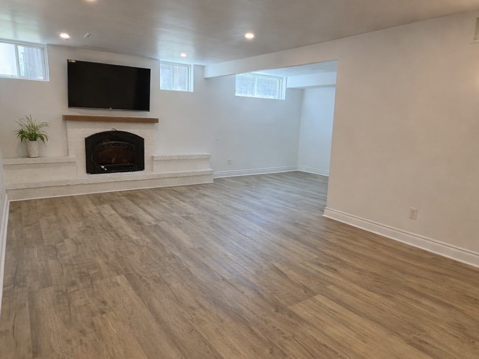 Finished basement renovation in West Island Montreal featuring a modern fireplace, wall-mounted TV, luxury vinyl flooring and bright open layout
